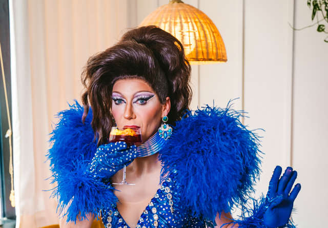Drag Queen in a blue statement outfit drinking a cocktail at Virgin Hotels.