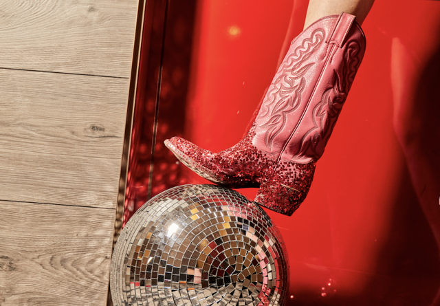 Red glitter cowboy boot on a disco ball against a vibrant red backdrop, highlighting bold and playful decor.