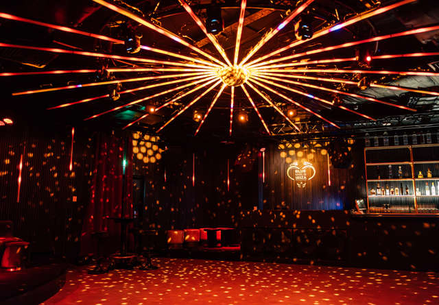 Vibrant nightclub with a golden disco ball and dynamic red and orange lighting reflecting across the dark space.